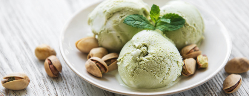 white bowl of pistachio ice cream with whole pistachios surrounding it