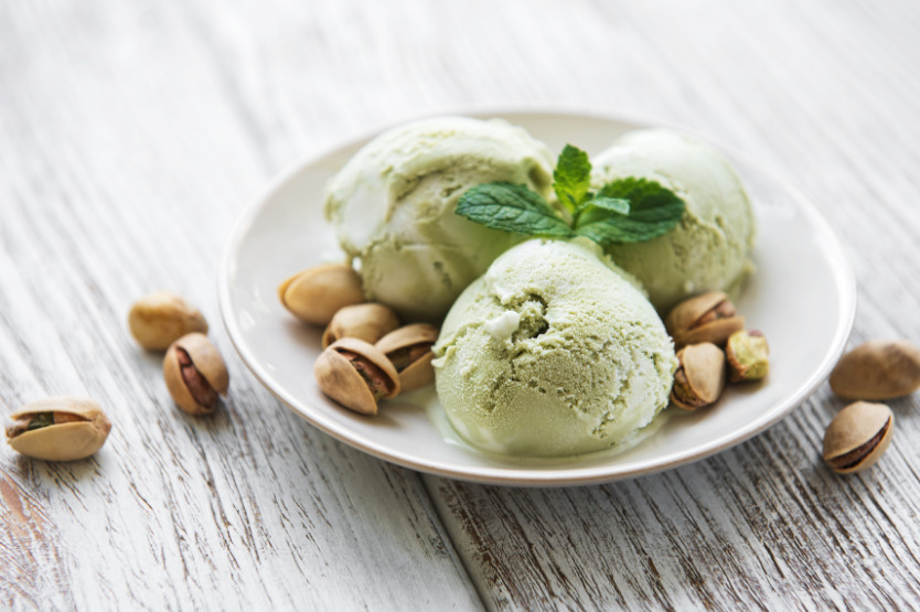 white bowl of pistachio ice cream with whole pistachios surrounding it